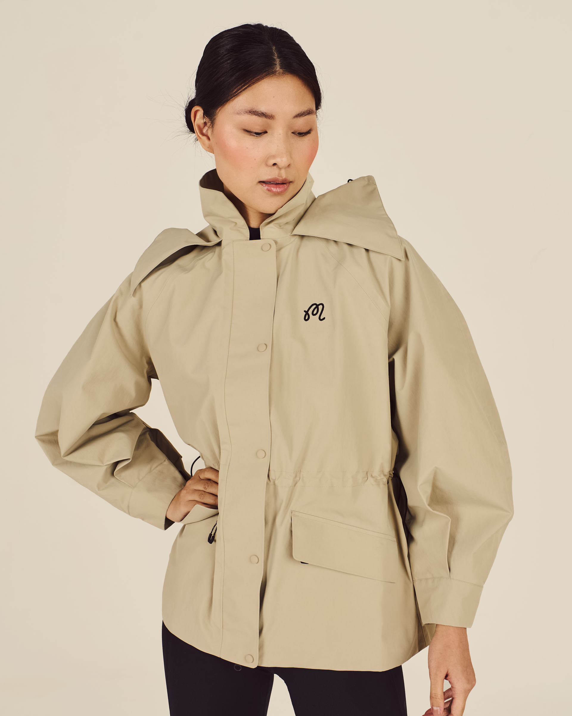 Woman wearing a beige jacket with a brand logo on a beige background