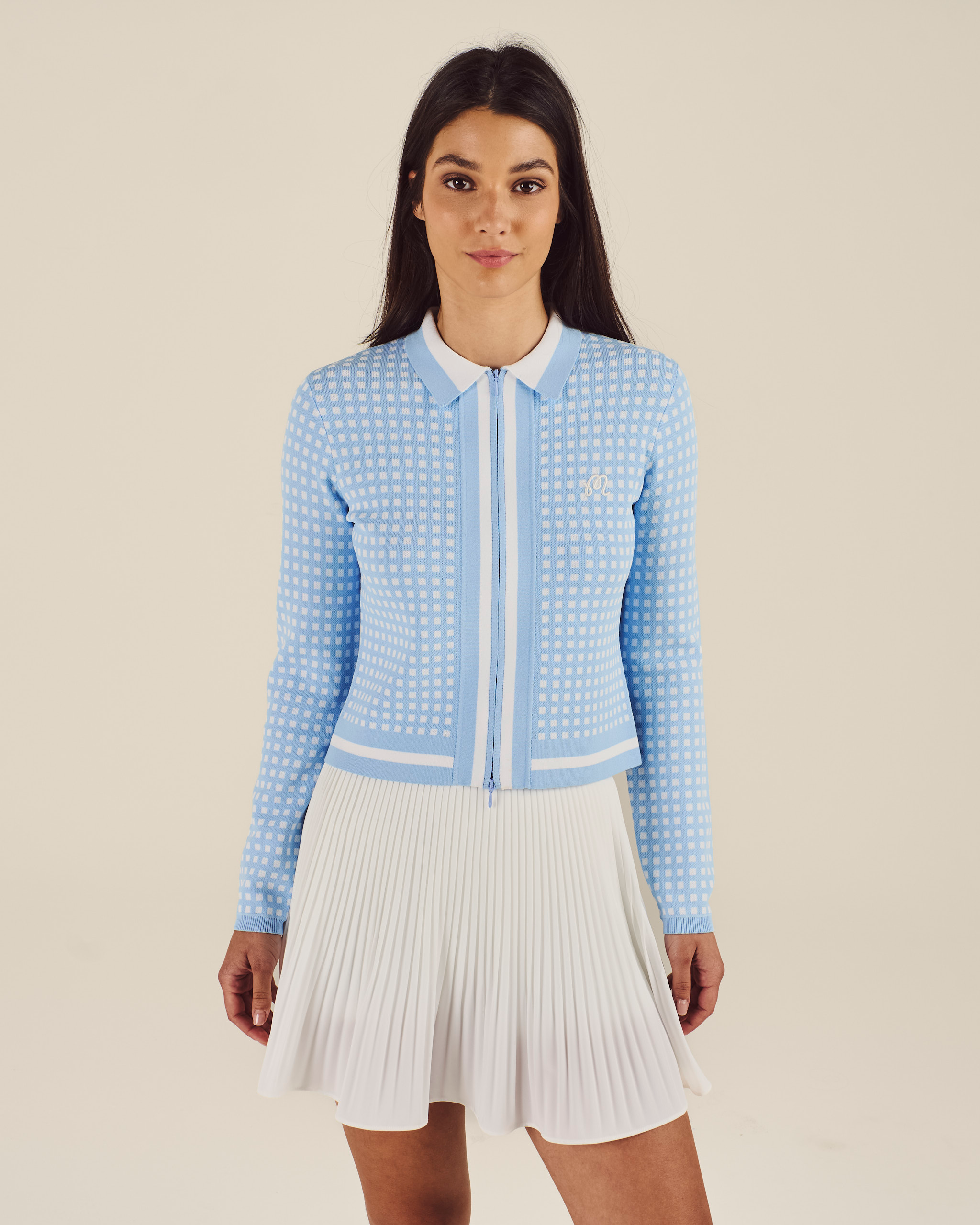 Woman wearing a light blue textured jacket and white pleated skirt on a beige background