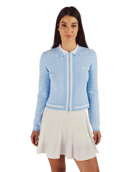 Woman wearing a light blue textured jacket and white pleated skirt on a beige background