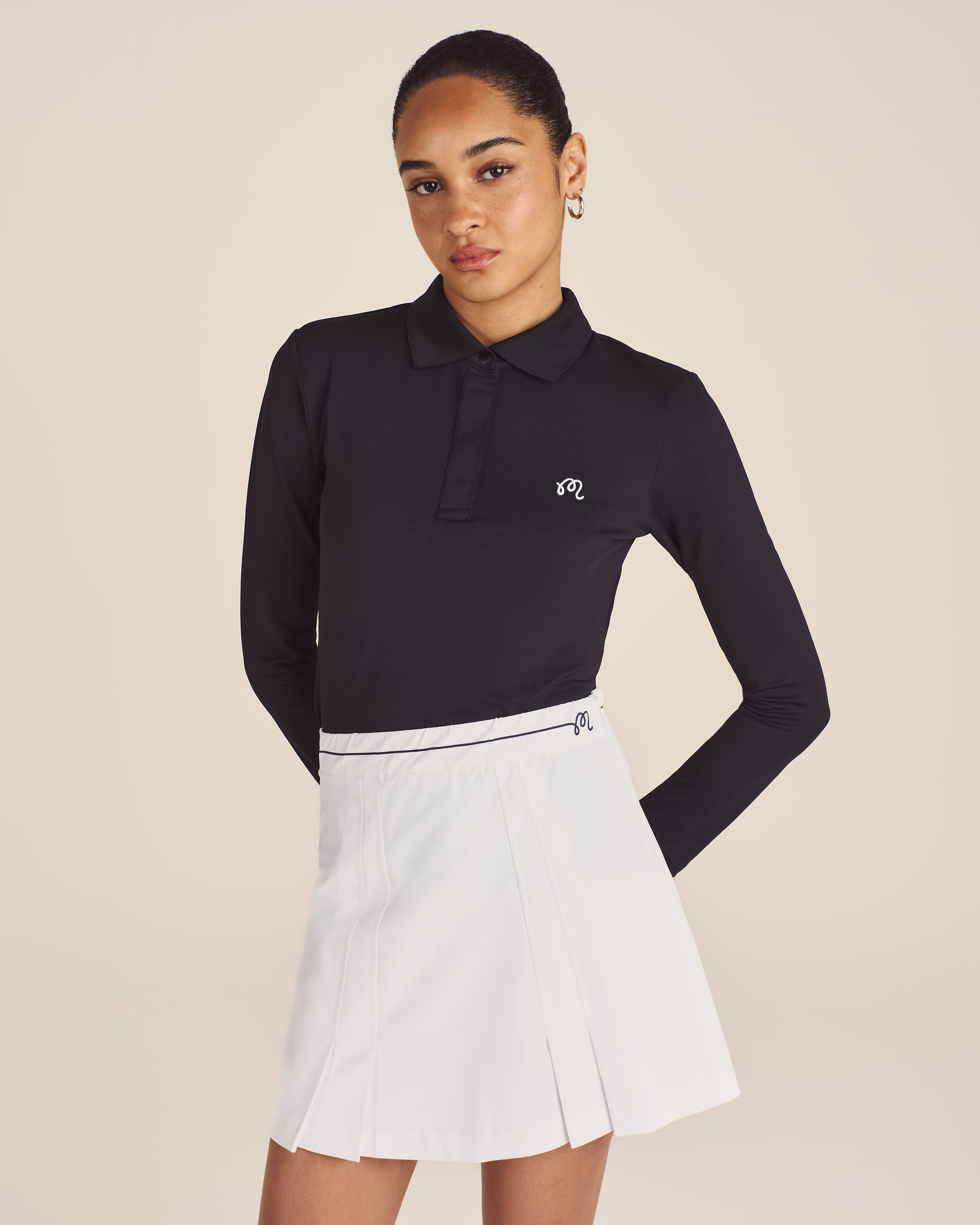 Woman wearing a black long-sleeve polo shirt and white skirt on a beige background