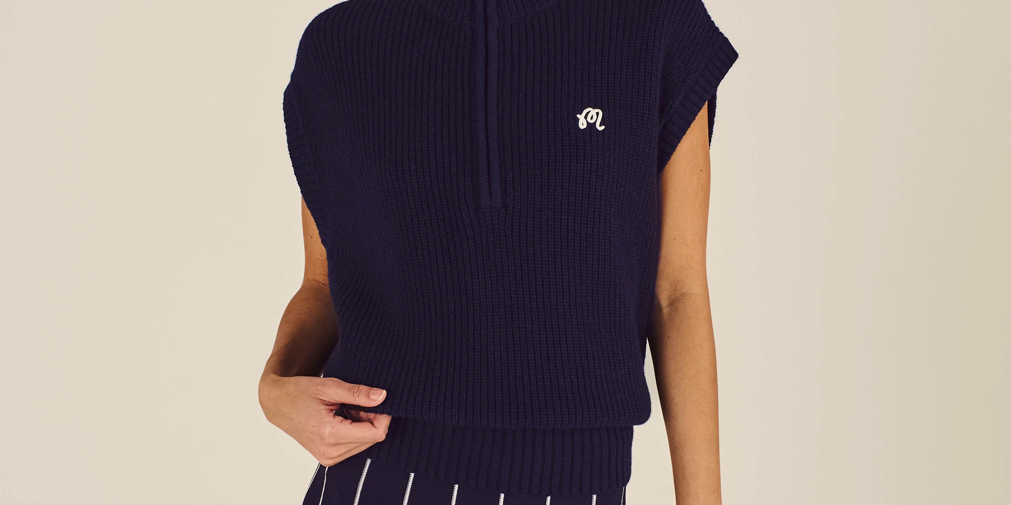 Woman wearing a navy sleeveless sweater and pleated skirt on a beige background