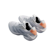 White tennis shoes with orange accents on a blue surface with a tennis racket and ball.