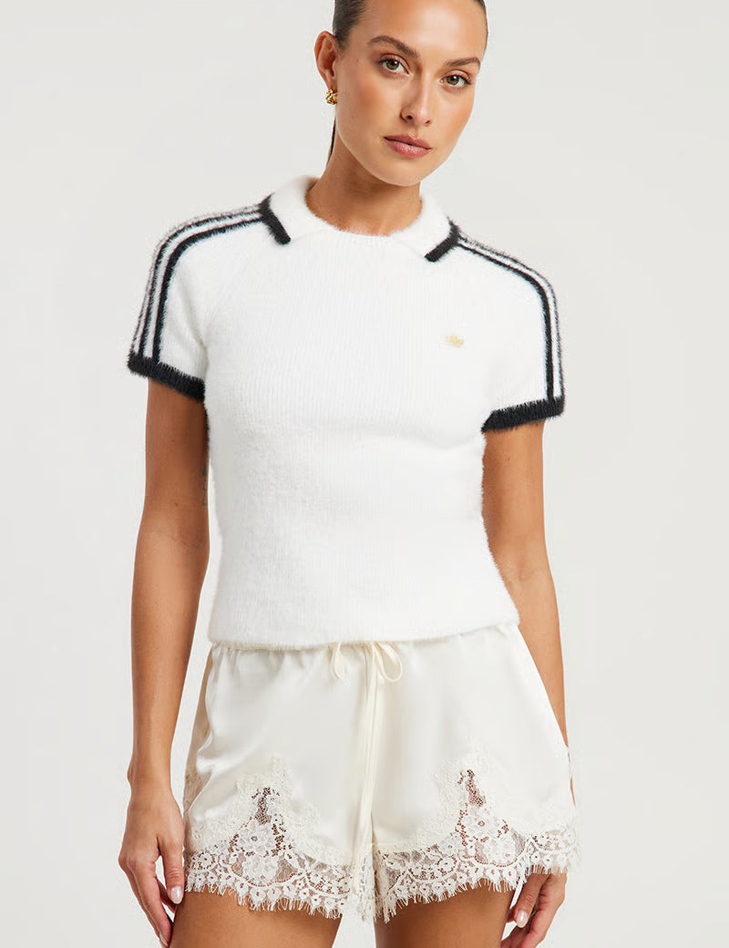 Woman wearing a white top with black trim and lace shorts on a white background