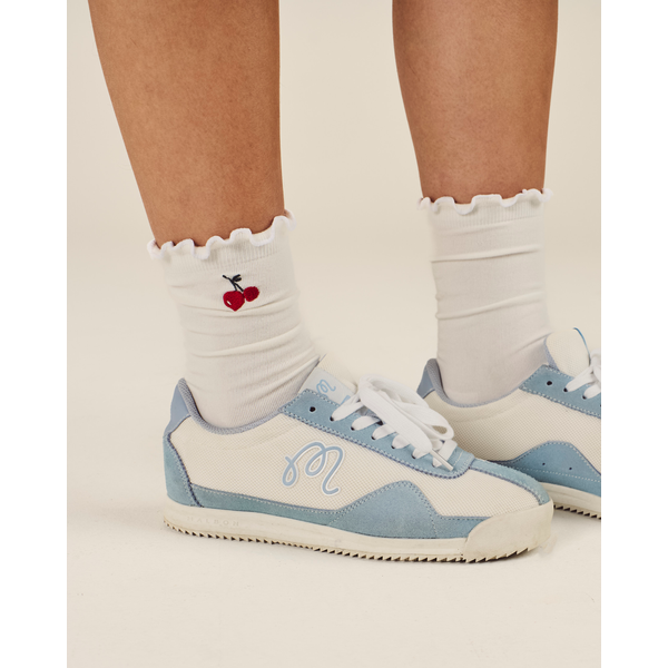 White sneakers with blue accents worn with white socks featuring a red cherry design.